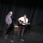 two men on stage tuning a guitar